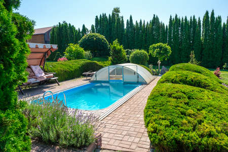 Swimming pool and garden with nicely trimmed bushes and stones in backyard. Landscape design. High quality photoの写真素材
