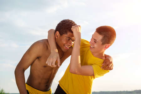 Two African-American and Caucasian friends have fun, fight and laugh outdoors by the river in summerの写真素材