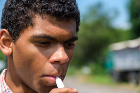 Close up face of young black african american man smoking electronic cigarette with e-liquid...