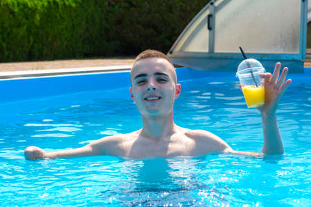 Young smiling guy with an amputated arm drinks a cocktail in swimming pool in the courtyard of his houseの写真素材