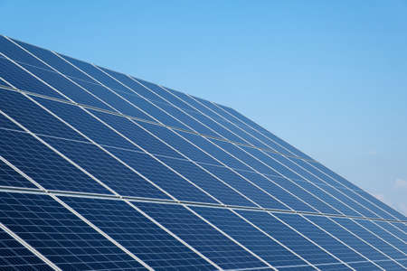 Row of solar panels on a solar farm under a blue sky. Solar power plant, an ecological alternative source of electricity. Side view, copy spaceの写真素材