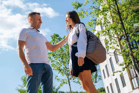Back to school. Caucasian schoolgirl with backpack and uniform hugs her smiling father on the street before going to school.の写真素材