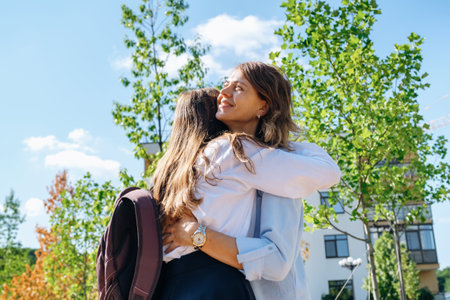 Back to school. Caucasian pupil girl with backpack and uniform hugging her smiling mother on the street before go to the school.の写真素材