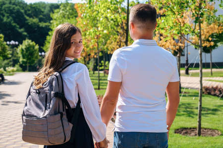 Daughter in school uniform and father walking together to school down the street, holding hands, back viewの写真素材