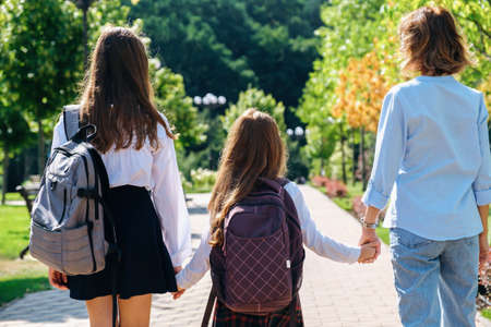 Two daughters in school uniform walking together with mother to school down the street, holding hands, back viewの写真素材