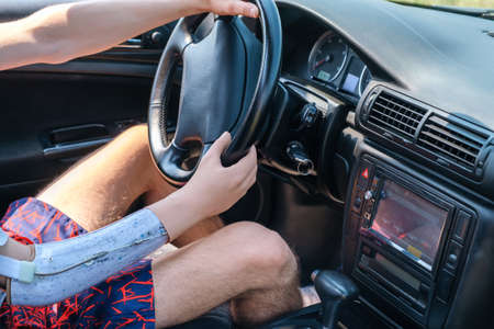 Prosthetic amputated hand of a Caucasian man on the steering wheel who drives a car on a sunny summer dayの写真素材