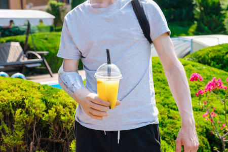 Caucasian man with amputated arm holding cocktail in prosthesis while standing on the lawn in the backyard of his houseの写真素材