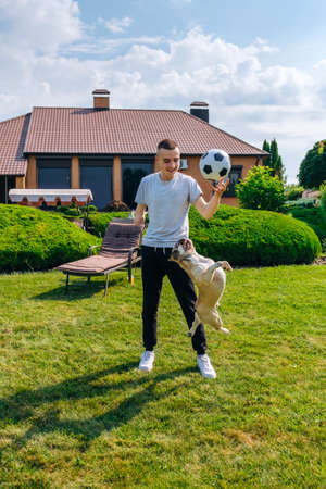Young caucasian man with amputated arm and prosthesis playing with his dog with a soccer ball in the backyard of his house, vertical orientationの写真素材