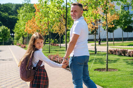 Daughter in school uniform and father walking together to school down the street, holding hands, back viewの写真素材