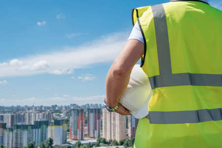 Builder, foreman or architect holds a white hard hat in his hand on the roof of a building under construction, rear view, copy spaceの写真素材
