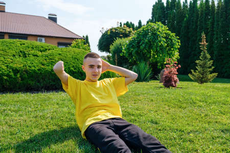 Young male with amputated arm doing abs exercise on lawn and looking at camera during rehabilitation session on sunny day in yardの写真素材