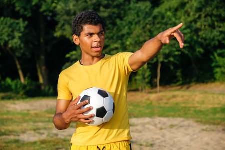 Young smiling Brazilian man holds a ball and pointing away with his finger before playing on a...