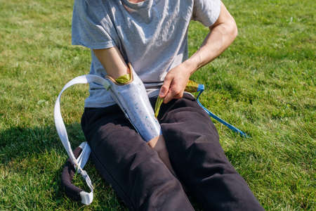 Young male with amputated arm puts on prosthesis while sitting on lawn on sunny day in yardの写真素材