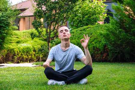 Young caucasian male with amputated arm meditating yoga in lotus pose outdoors in his backyard in summerの写真素材