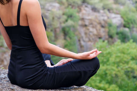 Crop unrecognizable female doing lotus pose while sitting on edge of rocky cliff in highlands during yoga training in natureの写真素材
