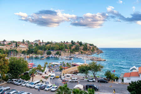 ANTALYA, TURKEY - OCTOBER 17, 2021: Cars parked on pier with residential buildings and green trees near rippling sea with moored boats on summer day in coastal Antalyaのeditorial素材