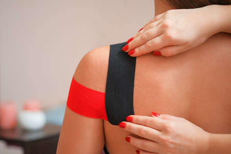 Female shoulder with applied red kinesiology tape and doctor hands close-upの写真素材