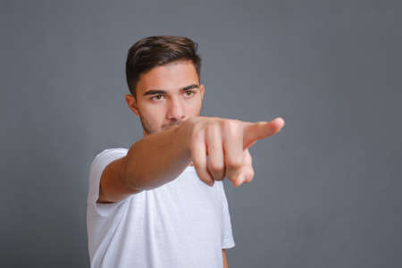 Handsome man in white t-shirt shows his index finger to the camera on a gray backgroundの写真素材