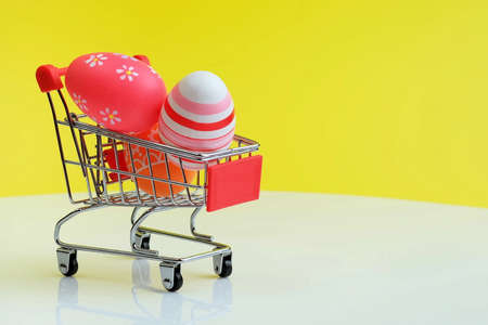 Shopping trolley with colorful painted Easter eggs, minimal holiday season concept, yellow background, copy spaceの写真素材