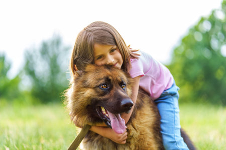Smiling little girl hugs a shepherd dog while sitting on its back in a summer park. High quality photo, close up viewの写真素材