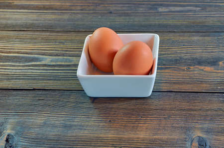 Chicken eggs in a square white clay plate on a wooden background. Side view, panorama. Food background, copy space. Concept of natural farm products.の写真素材