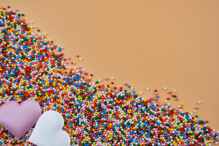 A mix of colorful sugar balls and hearts on a beige background with space for text. Festive...