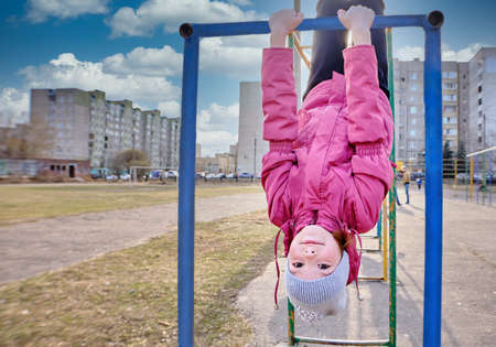Happy funny girl plays in the playground. A child does sports exercises on the stairs in the street against the blue sky. A teenager sports on the street. View from below.の写真素材