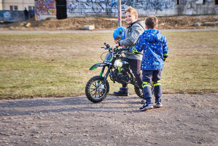 Two cheerful boys stand next to a motorcycle on a city street in the afternoon. Teenagers stand with a motorcycle in the school stadium.のeditorial素材