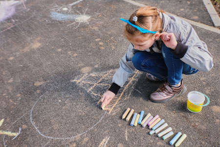 A happy girl draws with colorful crayons, Chalk on the asphalt, on the road on the street. High quality photoの写真素材