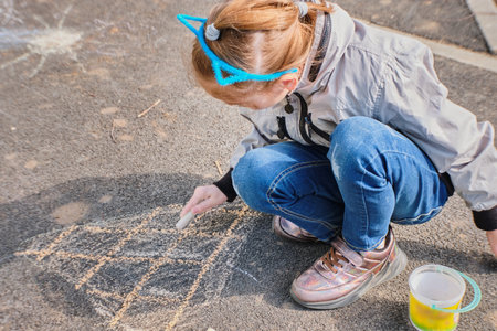 A happy girl draws with colorful crayons, Chalk on the asphalt, on the road on the street. High quality photoの写真素材