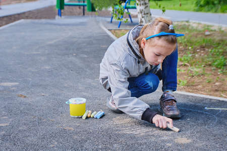 A happy girl draws with colorful crayons, Chalk on the asphalt, on the road on the street. High quality photoの写真素材