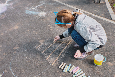 A happy girl draws with colorful crayons, Chalk on the asphalt, on the road on the street. High...