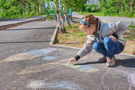 A happy girl draws with colorful crayons, Chalk on the asphalt, on the road on the street. High quality photoの写真素材