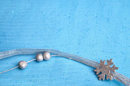 Christmas decoration on a blue background. Silver ribbon and silver beads lie on the fabric. Selective focus, close-up. A place to copy. High quality photoの写真素材