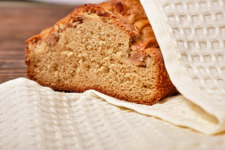 Sliced freshly baked homemade apple pie, covered with a beige napkin, towel on a brown wooden table....