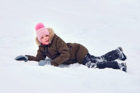 A happy smiling funny child, a girl walking outside in winter, playing with snow. A sunny winter day