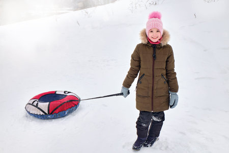 Active happy girl sliding down a snowy hill on a snow tubing, sledding in the park in the snowy air....