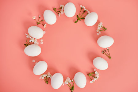 A frame of white flowers and white eggs on a pink background. Copy space, top view. Easter backgroundの写真素材