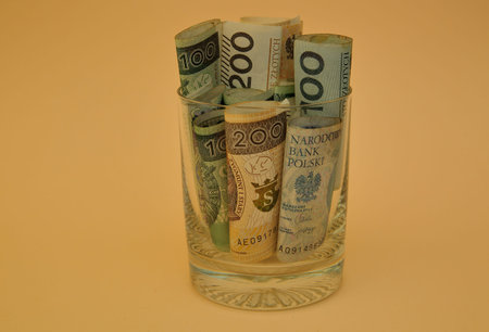 Banknotes of 200 and 100 Polish zloty rolled in rolls into glass close up isolated on yellow backgroundの写真素材