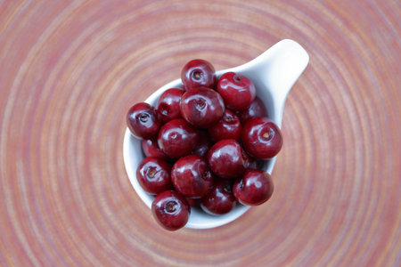 Fresh juicy cherries in bowl top view close up, background vibrant circle colorful