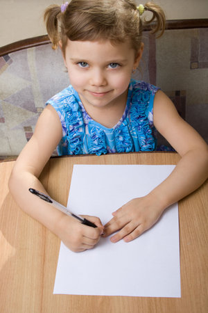 small girl learns to write sists at a tableの写真素材