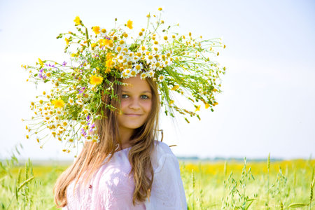 Young girl with camomile wreath on head stand on meadowの写真素材