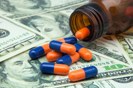 Open bottle of pills on top of moneyの写真素材