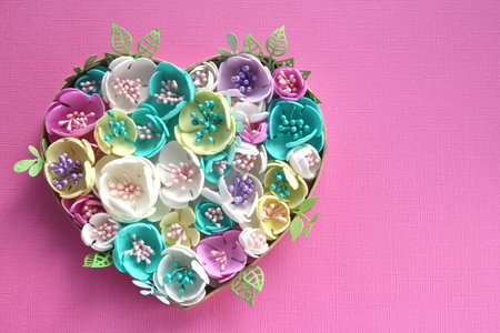 heart of artificial flowers handmade on a pink paper background. Copy space.