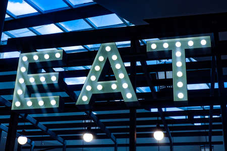 large inscription "EAT" with luminous bulbs under the ceiling on wooden boards.の写真素材
