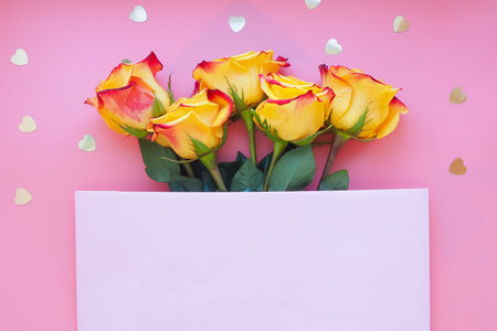 bouquet of five yellow-red roses and golden hearts on a pink background. A pink sheet of paper on...