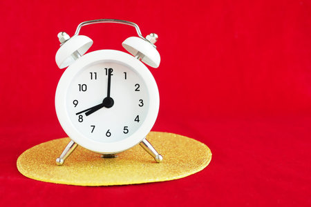 small white alarm clock on a golden shiny circle. Bright red background. copy space.