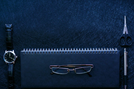 black office supplies: weekly on a spring, watches, pen, scissors and glasses on a black background....