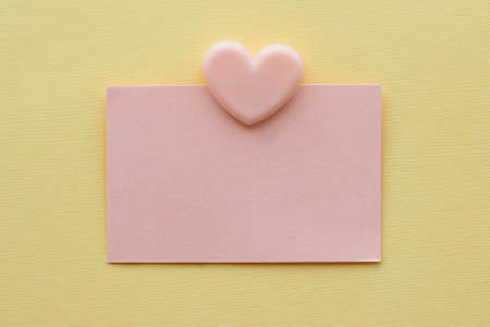 postcard pink rectangular sticker and pink clip in the form of a heart on a yellow background. minimalistic background. space for text.の写真素材
