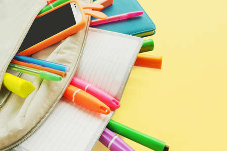 Colored bright markers, pens, sharpener, eraser, scissors, stick out from under the notebook in different directions and the inscription in multi-colored letters in Russian "school is coming"の写真素材